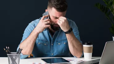 Personne au bureau avec téléphone, lunettes et ordinateur.