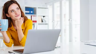 Personne tenant une tasse, rêvant devant un ordinateur portable.