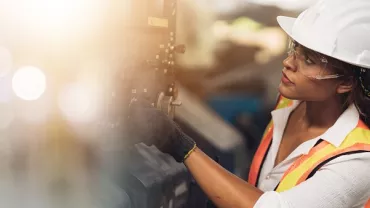 Travailleur en gilet réfléchissant et casque inspectant une machine en usine.