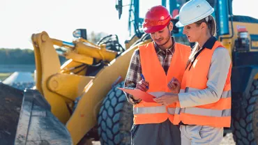 Deux personnes en gilets de sécurité discutant sur un chantier.